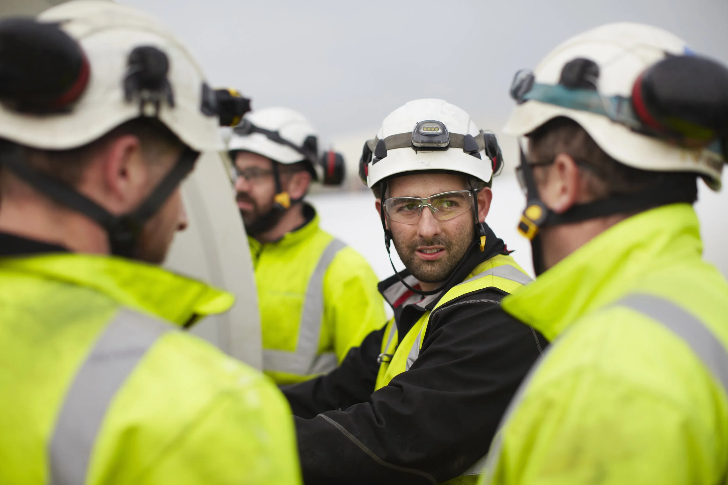 Group of construction workers in safety gear and high visibility jackets having a discussion at a worksite.