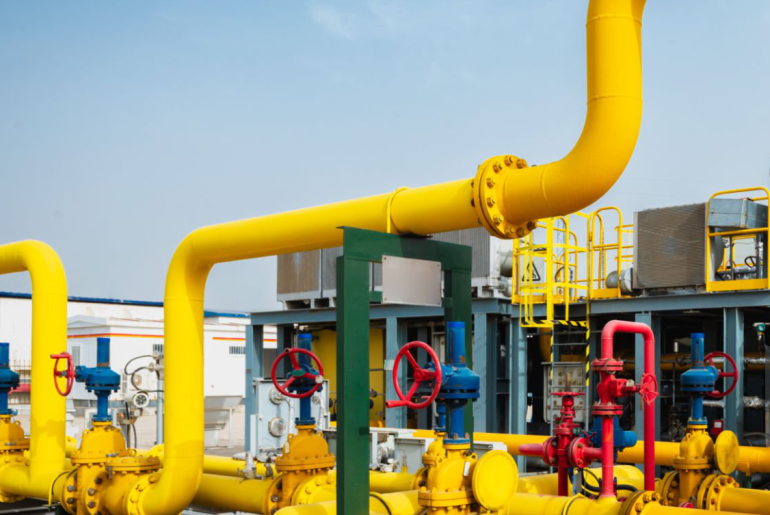 Industrial oil or gas pipeline system with yellow and red pipes with valves, outdoors, blue sky background