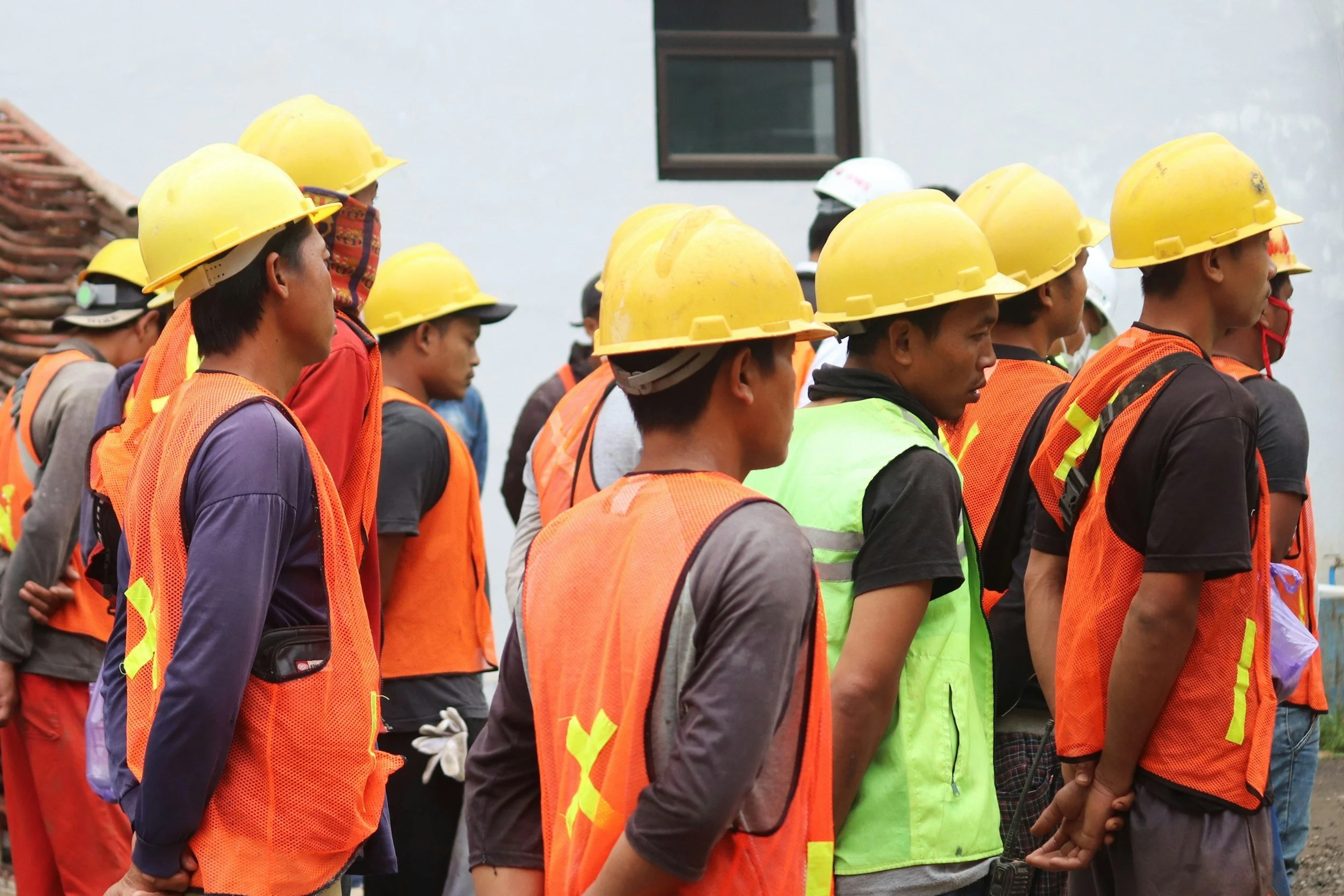 Construction workers wearing yellow hard hats and orange safety vests, standing in a group.