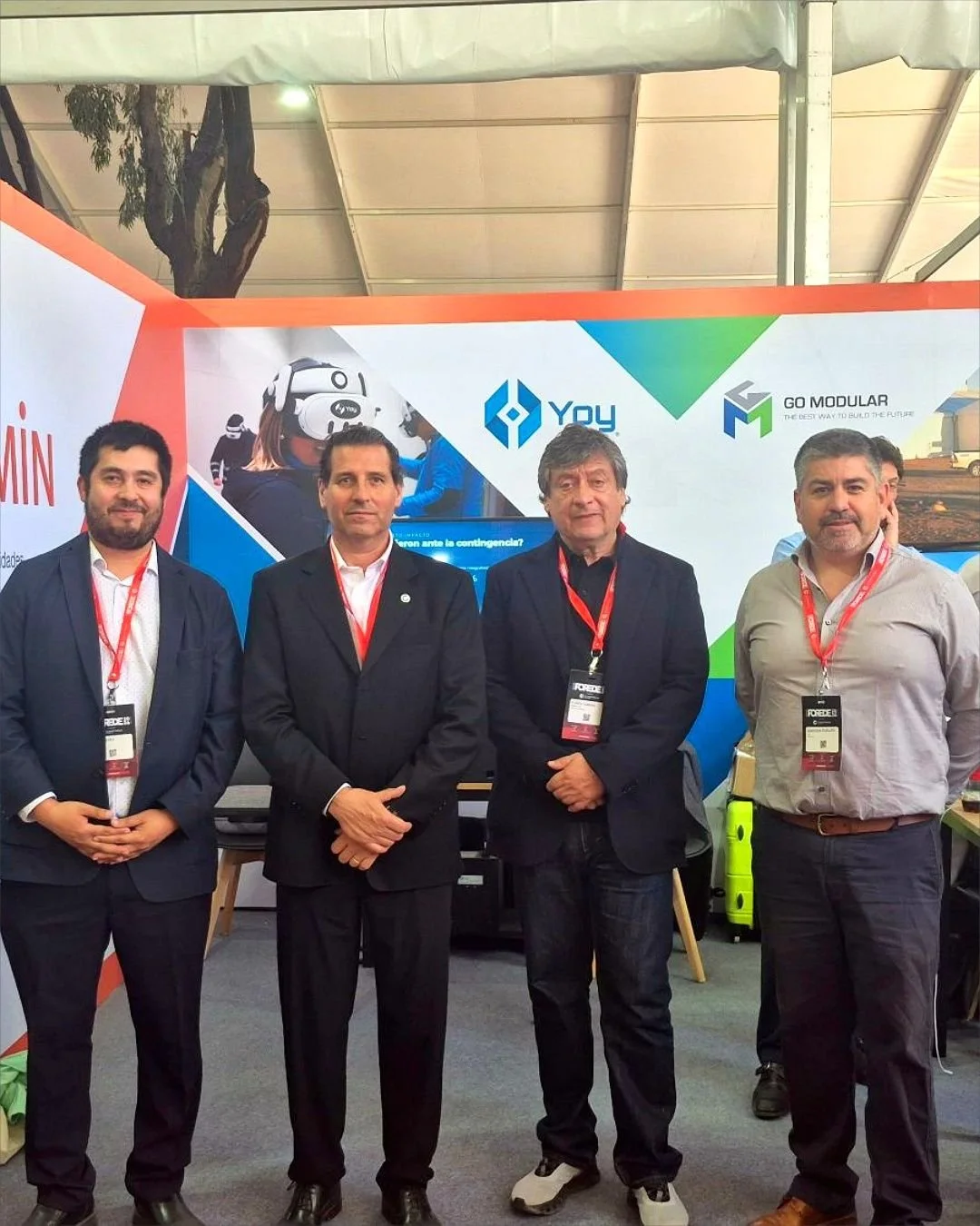 Cuatro asistentes con credenciales de la feria posan frente al stand de Yoy Simulators en Expo FOREDE 2026.