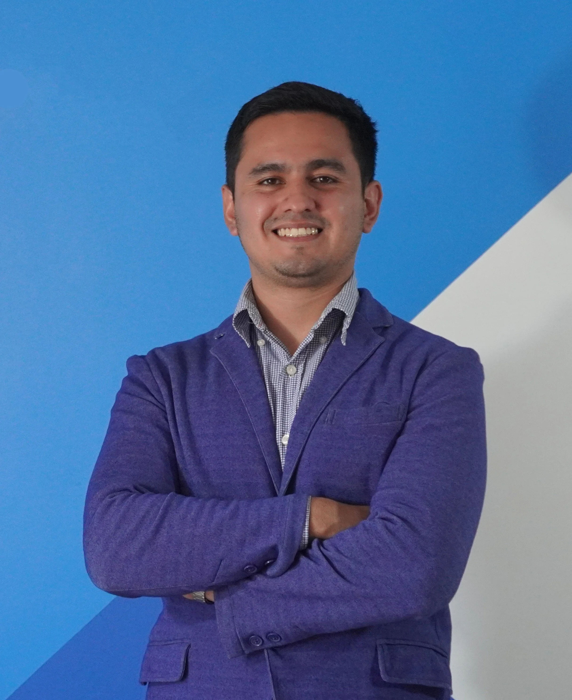 Piero Ampuero in a blue blazer smiling with arms crossed against a blue and white background.