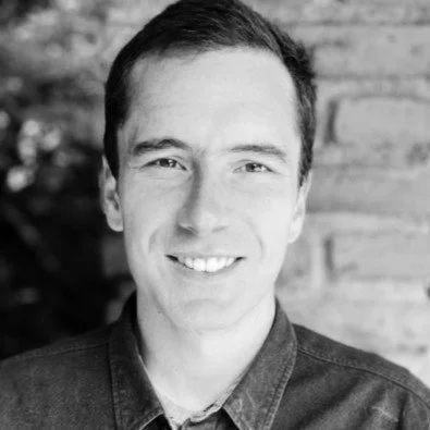 Black and white portrait of a smiling person in front of a brick wall.