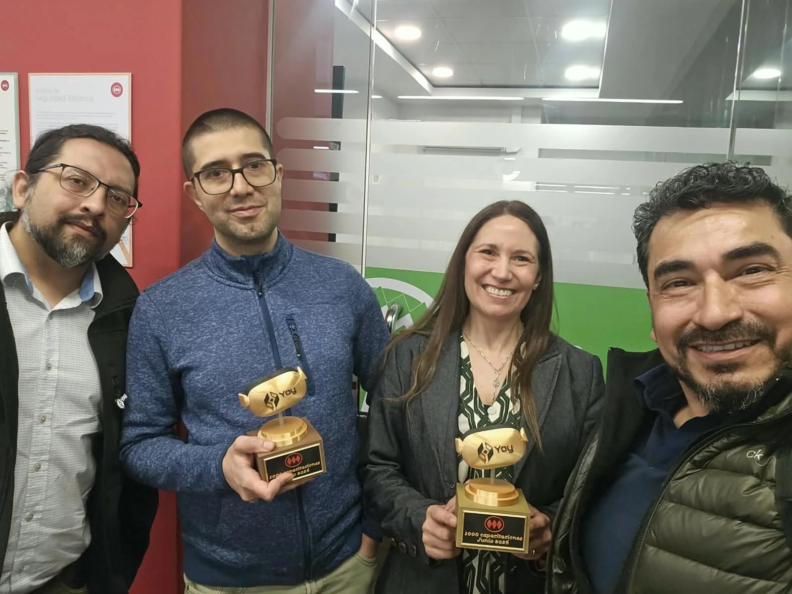 Cuatro personas en las oficinas de Metro de Santiago; dos de ellas sostienen trofeos dorados de Yoy por 1.000 capacitaciones.