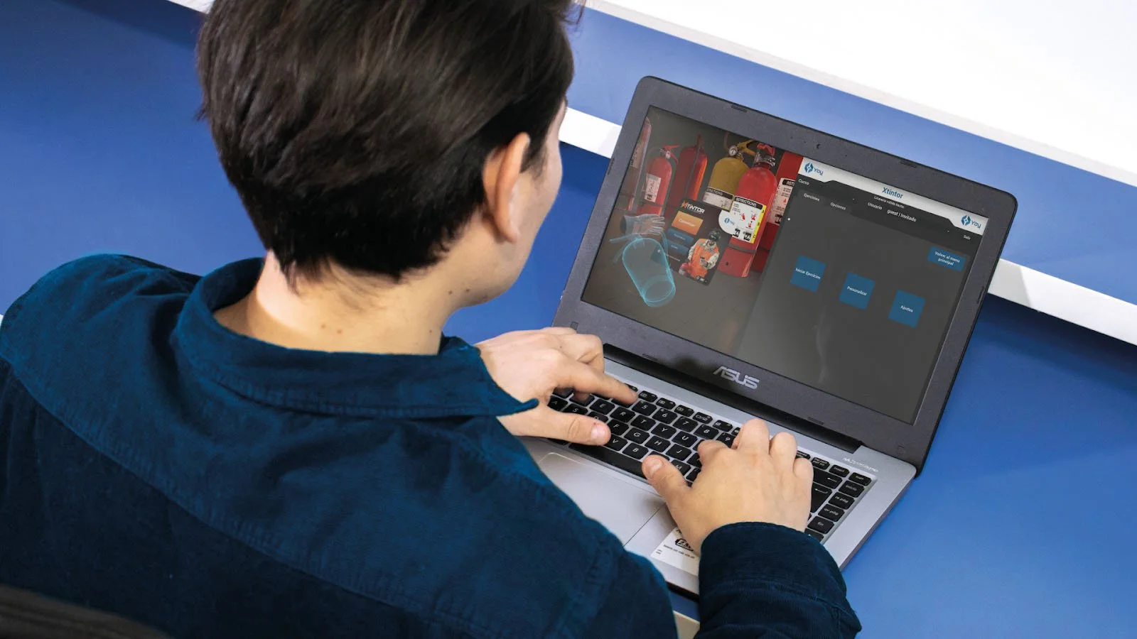 Persona usando un laptop con una simulación de realidad virtual en pantalla, relacionada con extintores y capacitación en seguridad.