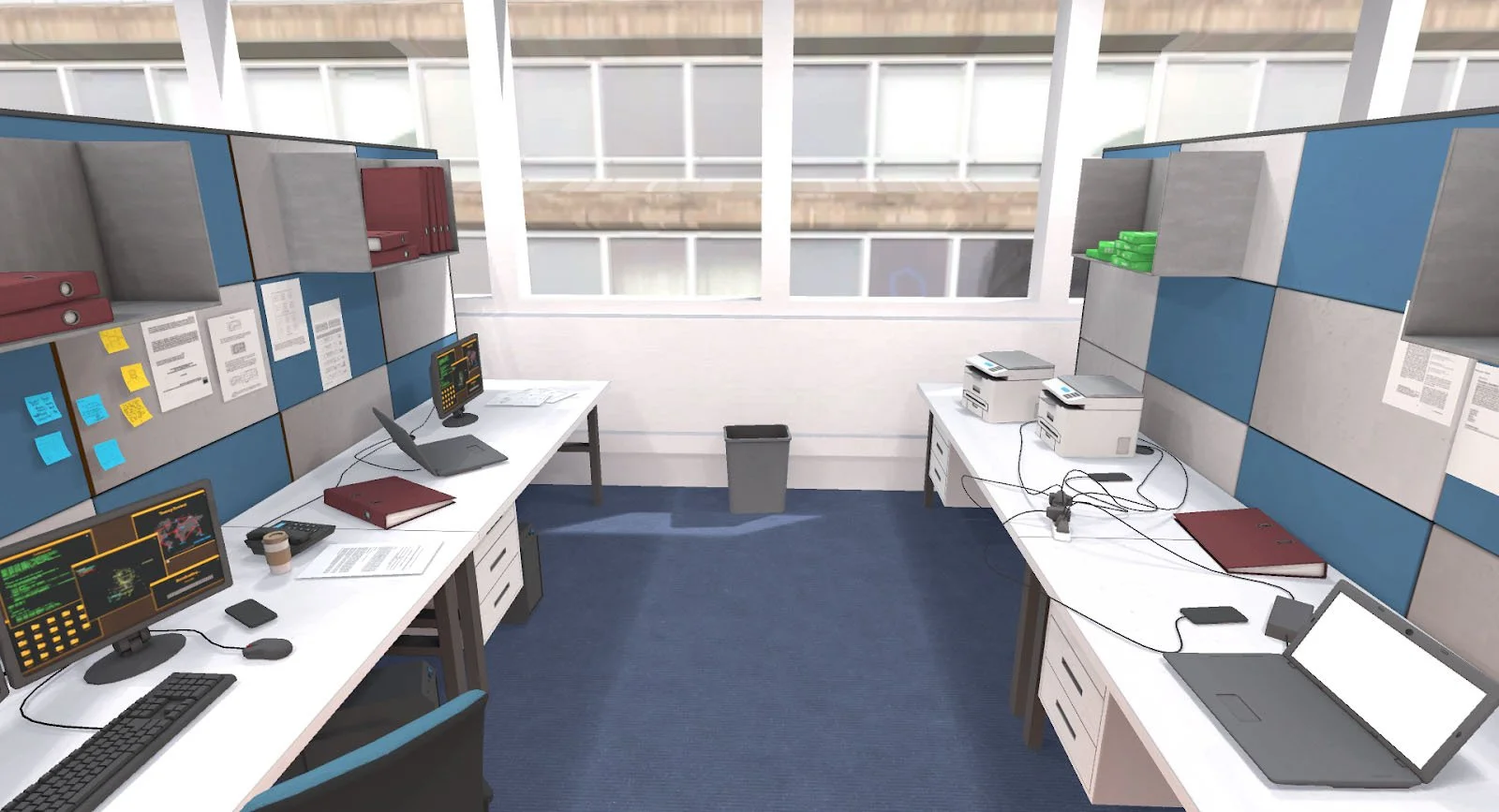 Interior de una oficina con dos escritorios, cada uno equipado con laptops y monitores. Un escritorio tiene una carpeta, una taza de café y documentos, mientras que el otro tiene cables, impresoras y más carpetas. El espacio incluye paneles divisorios azules y grises con estanterías y ventanas de fondo.