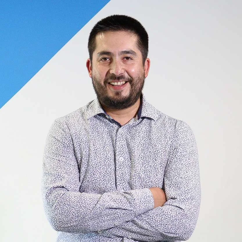 Juan Reyes with a beard in a patterned shirt, arms crossed, standing against a blue and white background.