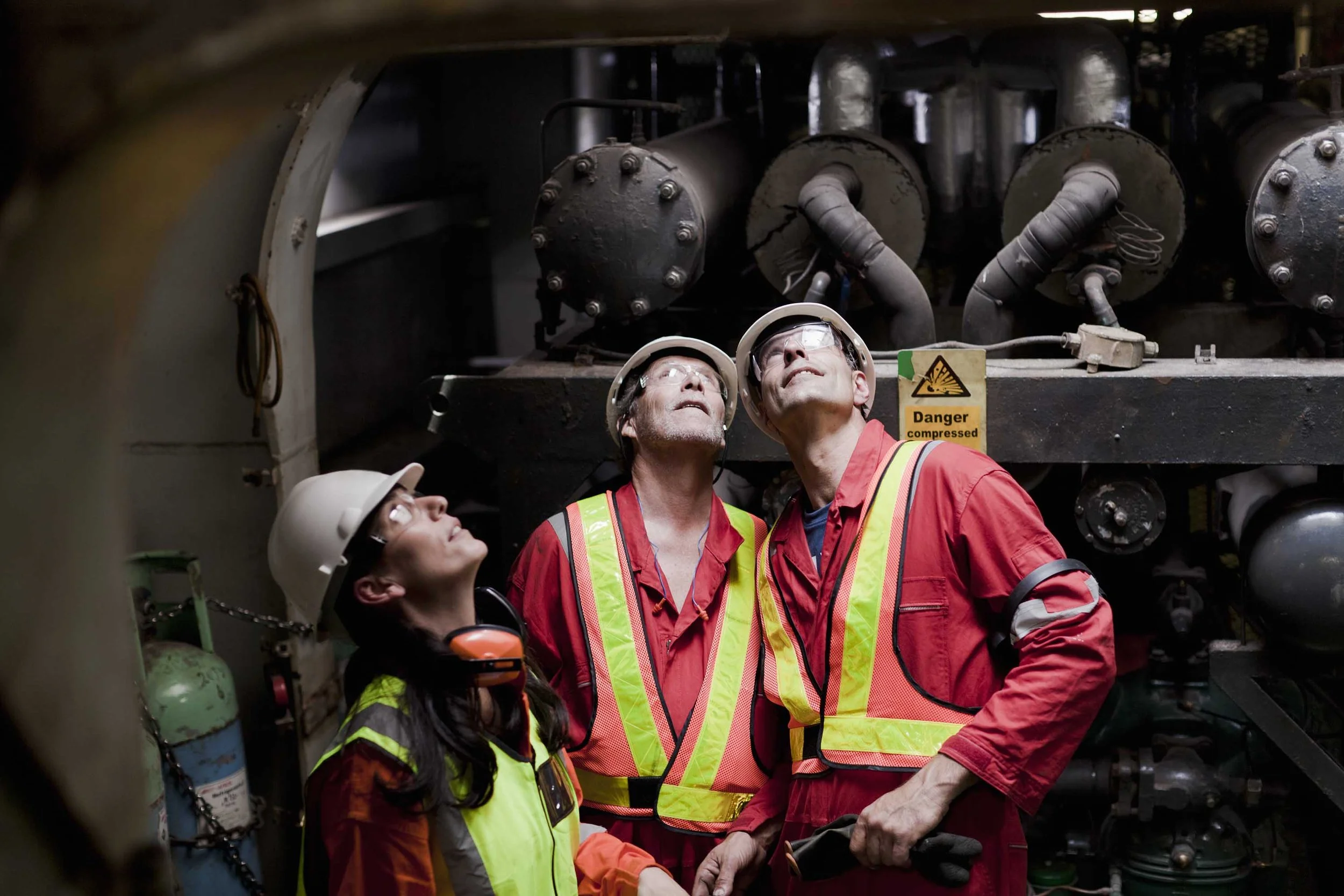 Trois travailleurs industriels en équipement de sécurité inspectant des machines.