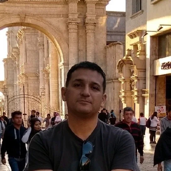 Man in black shirt in front of a stone archway on a busy street.